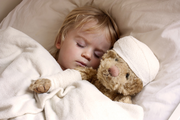 Das Bild einen kleinen Jungen, der mit seinem Teddy im Bett liegt. 