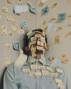 Das Bild symbolisiert Stress. In einer Ecke steht ein Mann, über den unzählige Notizzettel mit Aufgaben einprasseln.