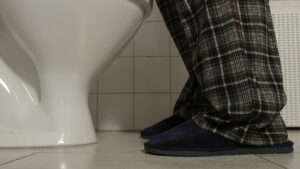 Closeup von männlichen Beinen in einer karierten Pyjama Hose und Hausschuhe, der nachts vor einer Toilette steht