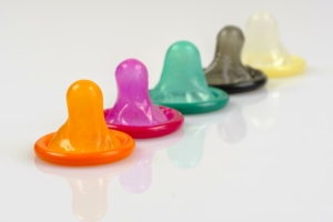 Das Bild zeigt fünf farbige Kondome (orange, pink, grün, schwarz und weiß). 
