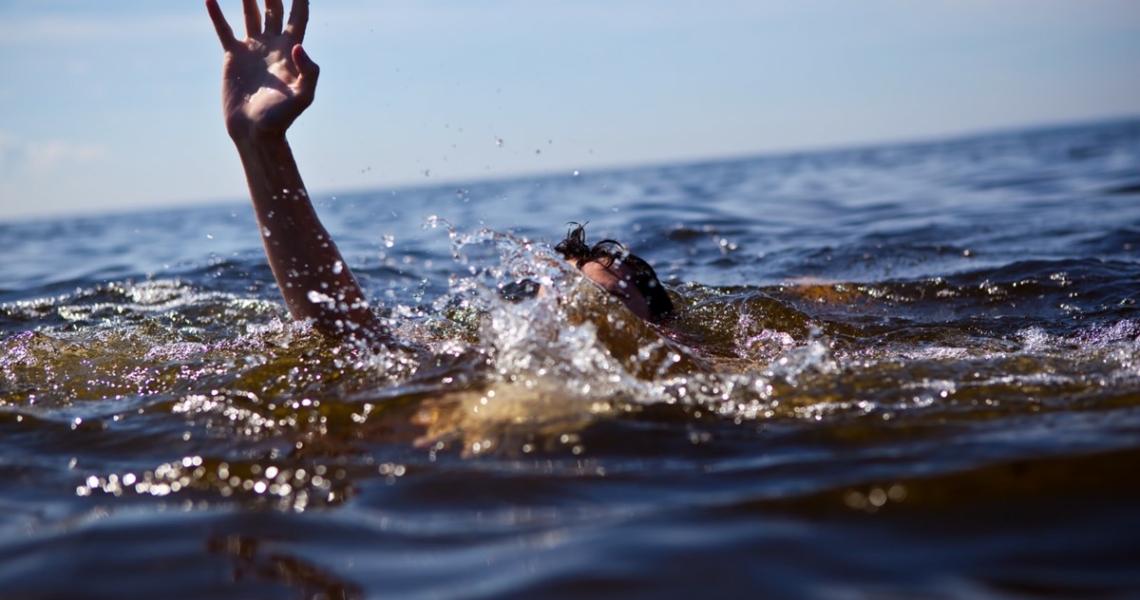 Eine Person ist im Wasser und scheint zu ertrinken. Man sieht wie eine Person ihre Hand hilfesuchend aus dem Wasser reicht.