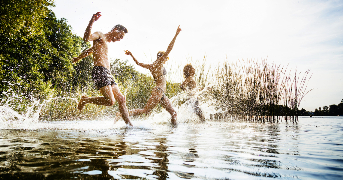 Das Bild zeigt eine Freundesgruppe läuft glücklich an einem Sommertag auf den See zu.