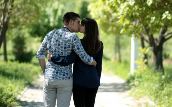 Das Bild zeigt einen Mann und eine Frau, die sich auf einem Weg im Grünen küssen. 