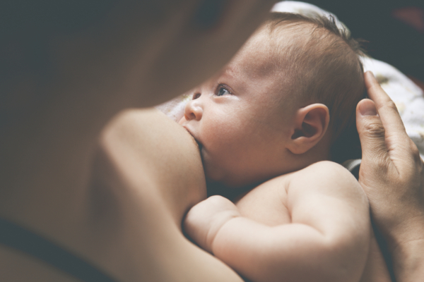Das Bild zeigt ein Baby, das an der Brust seiner Mutter trinkt