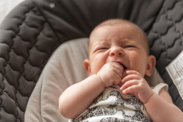 Das Bild zeigt ein weinendes Baby, welches sich die Finger in den Mund steckt. 