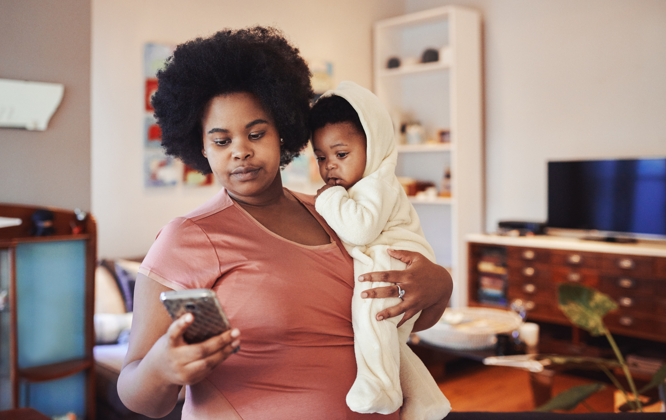 Eine Frau hält ihr Baby auf dem Arm und in der anderen Hand ein Smartphone.