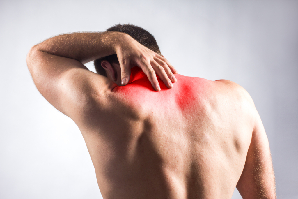 Ein Mann, der mit nacktem Rücken, der sich vor Schmerzen den Nacken hält.