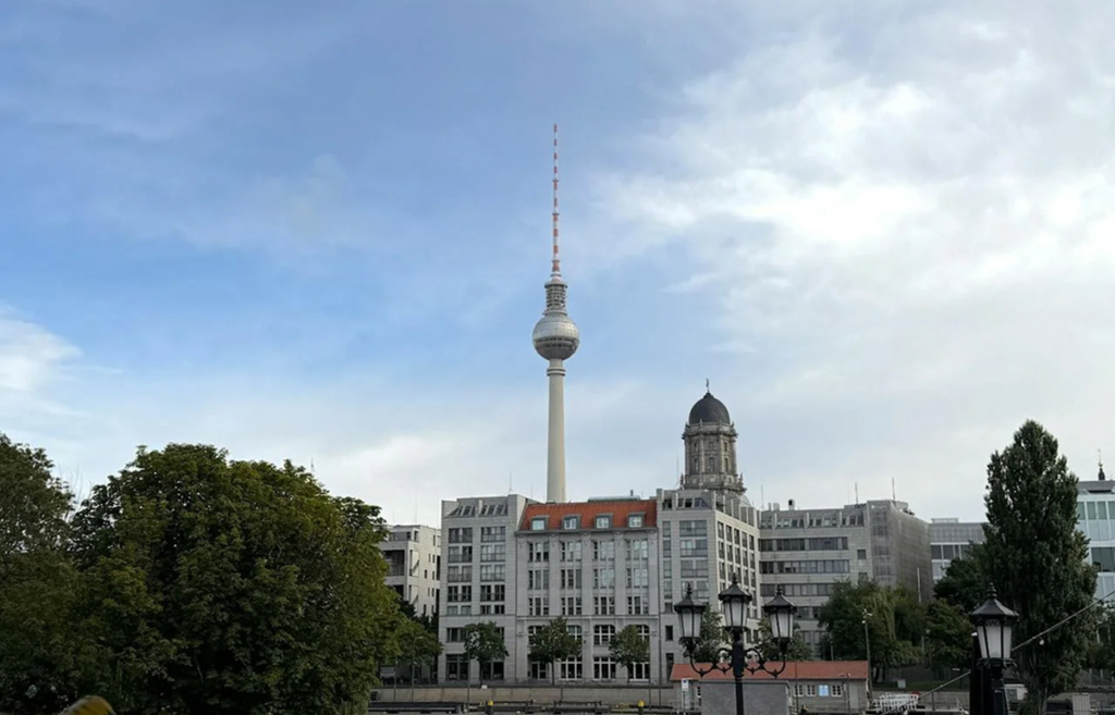 Fernsehturm Berlin vor blauem Himmel, umgeben von historischen Gebäuden und Bäumen. Hauptattraktion der Stadt.