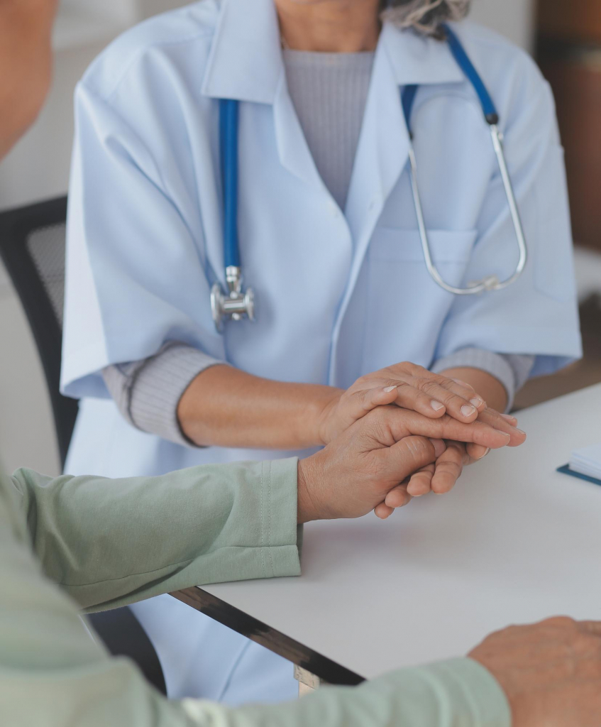 Arzt hält Patientens Hände am Tisch. Medizinische Unterstützung und Vertrauen. Stethoskop im Hintergrund.