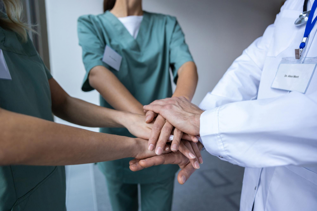Ärzte und Pflegekräfte stapeln ihre Hände als Zeichen der Teamarbeit im Krankenhaus.