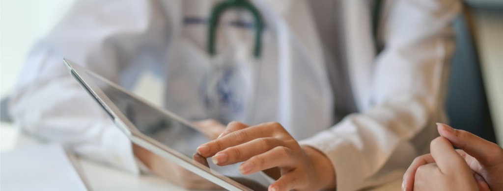 Arzt oder Ärztin in weißem Kittel nutzt ein Tablet zur Patientendatenverwaltung im medizinischen Umfeld.